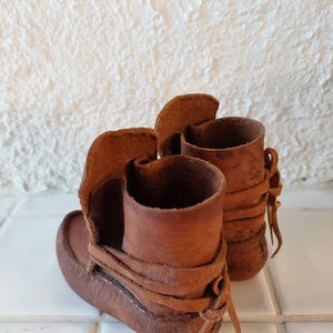 May include: A pair of brown leather moccasins with laces. The moccasins are tied at the ankle and have a fringe detail.