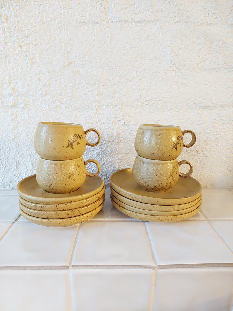 May include: Set of six yellow ceramic teacups and saucers with a textured surface and floral design. The cups and saucers are stacked on top of each other.