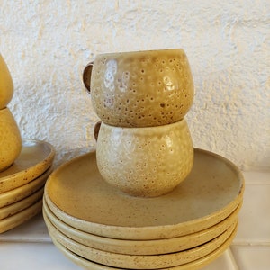 May include: A stack of four yellow ceramic saucers with a pair of matching yellow ceramic cups stacked on top of the saucer.