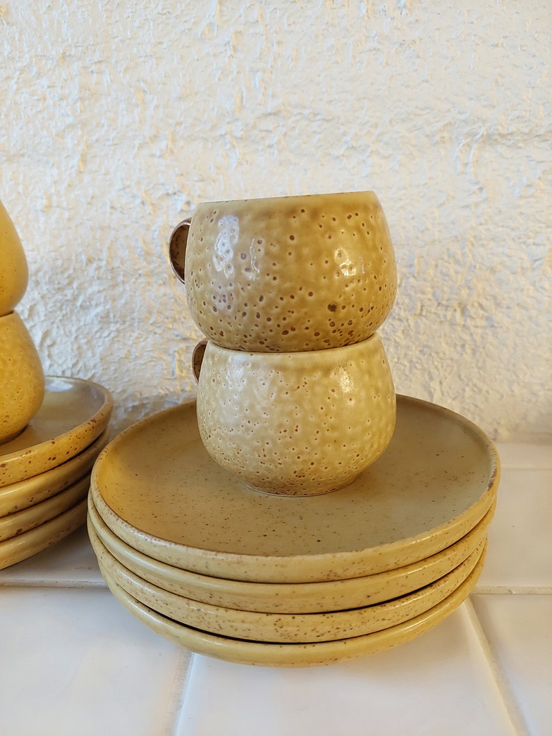 May include: A stack of four yellow ceramic saucers with a pair of matching yellow ceramic cups stacked on top of the saucer.