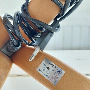 Może przedstawiać: Zbliżenie na drewnianą podstawę lampy z czarnym kablem elektrycznym i etykietą z napisem "Max 100 W 4008 B Wyprodukowano w Szwecji".