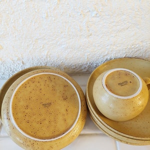 May include: A set of four yellow speckled ceramic plates and a matching cup with the text "Fentik Holland" on the bottom.