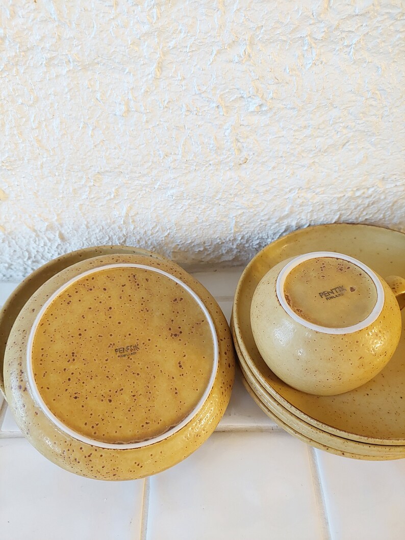 May include: A set of four yellow speckled ceramic plates and a matching cup with the text "Fentik Holland" on the bottom.