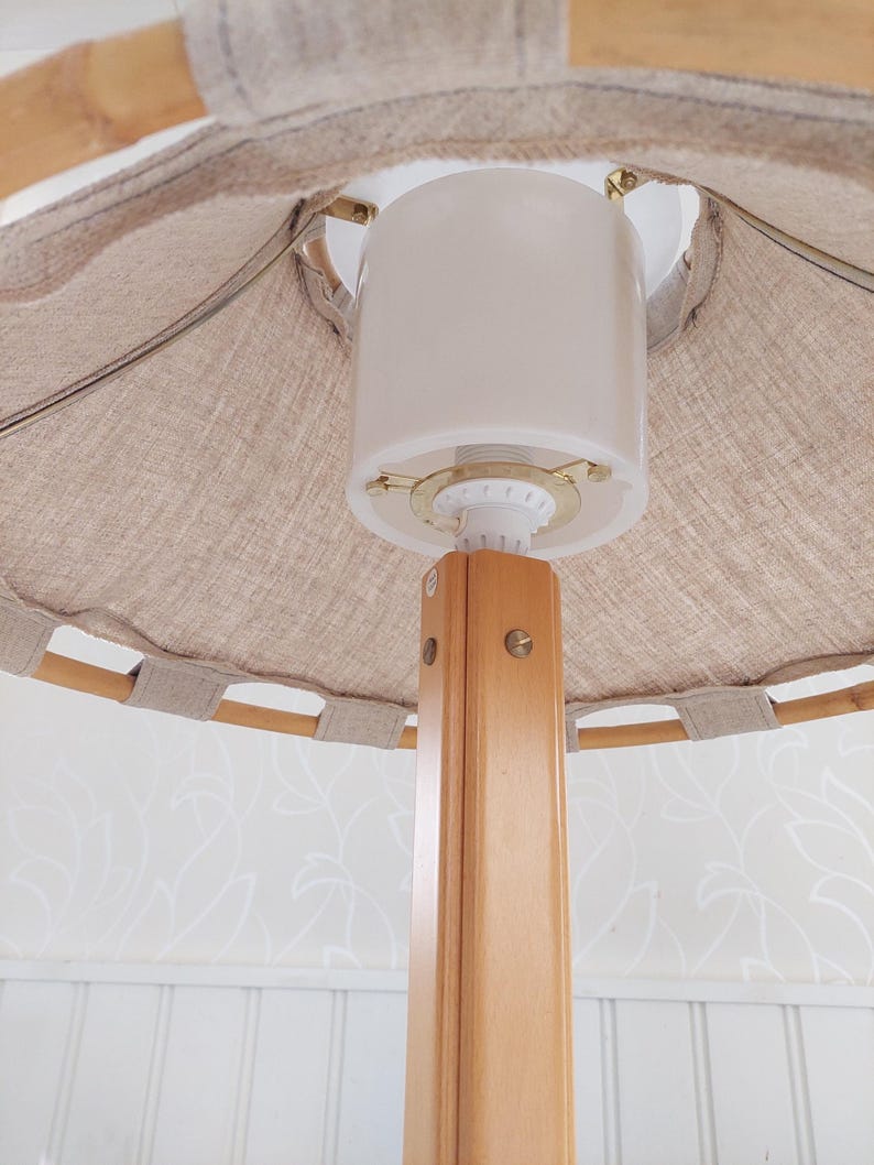 Może przedstawiać: Drewniana lampa stojąca z białym abażurem z tkaniny. Lampa ma prosty design i jest wykonana z naturalnych materiał&oacute;w.