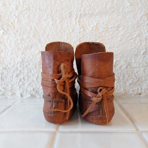 May include: A pair of brown leather ankle boots with laces. The boots are tied with a criss-cross pattern and have a worn look.