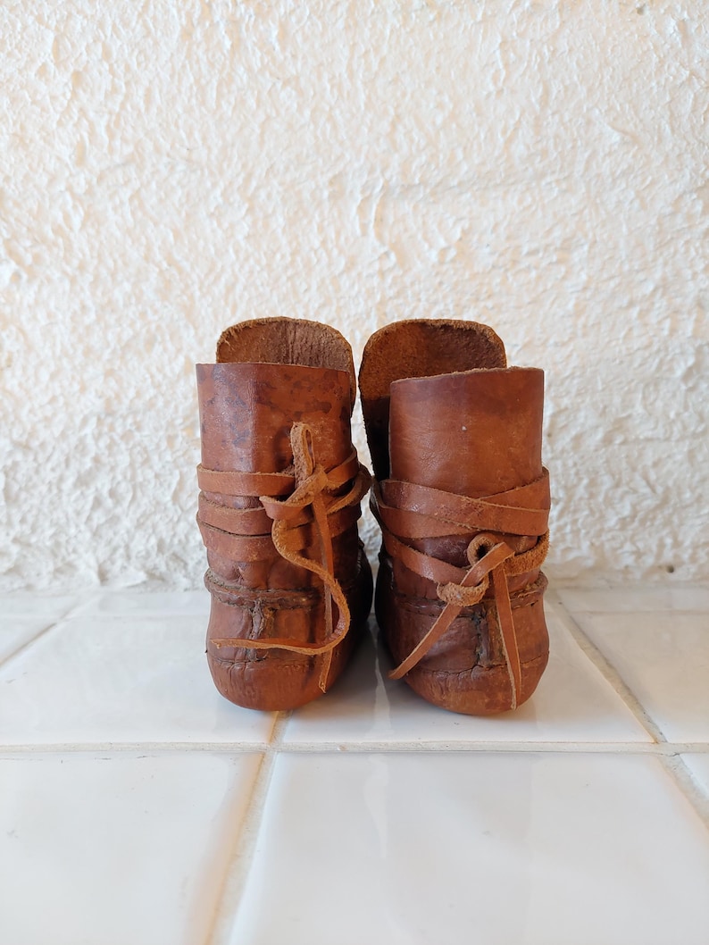 May include: A pair of brown leather ankle boots with laces. The boots are tied with a criss-cross pattern and have a worn look.