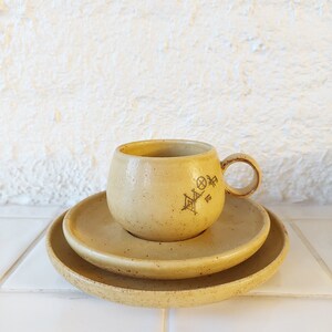 May include: A set of two yellow ceramic saucers and a matching cup with a brown geometric design.