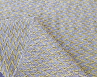 May include: A yellow and gray woven throw blanket with a diamond pattern. The blanket is folded in half and the texture of the weave is visible.