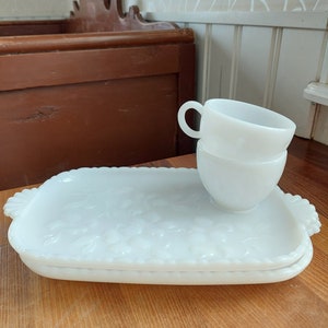 Può includere: Un vassoio da portata in vetro di latte bianco con un motivo floreale e un set di tre tazze in vetro di latte bianco.