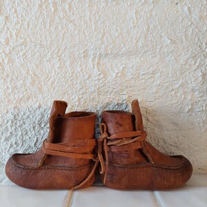 May include: A pair of brown leather moccasins with laces. The moccasins are tied together and have a worn look.