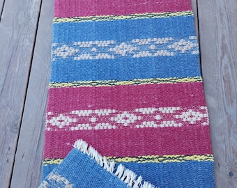 May include: A woven rug with blue, red, and yellow stripes. The rug has a fringe on the edges and is folded in half.