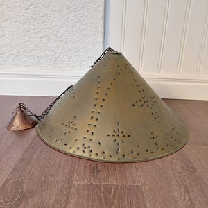 May include: A gold-toned metal pendant light fixture with a cone-shaped shade. The shade has a decorative pattern of small holes and stars. The light fixture is hanging from a chain.