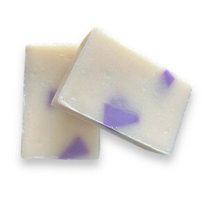 May include: Two bars of white soap with purple flecks. The soap is rectangular and has a smooth, glossy finish.