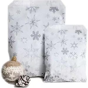 May include: Two white paper bags featuring a repeating silver snowflake pattern of various shapes and sizes. Beside the bags sits a round, textured beige and white ornament and a small, dark brown pinecone with white-tipped edges.