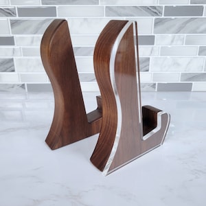 May include: Two wooden display stands with a curved design. The stands are made of dark brown wood with a silver-colored trim. The stands are designed to hold items for display.