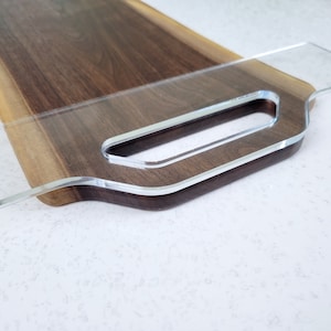 May include: A wooden serving tray with a clear acrylic handle. The tray is made of dark wood with a natural edge.