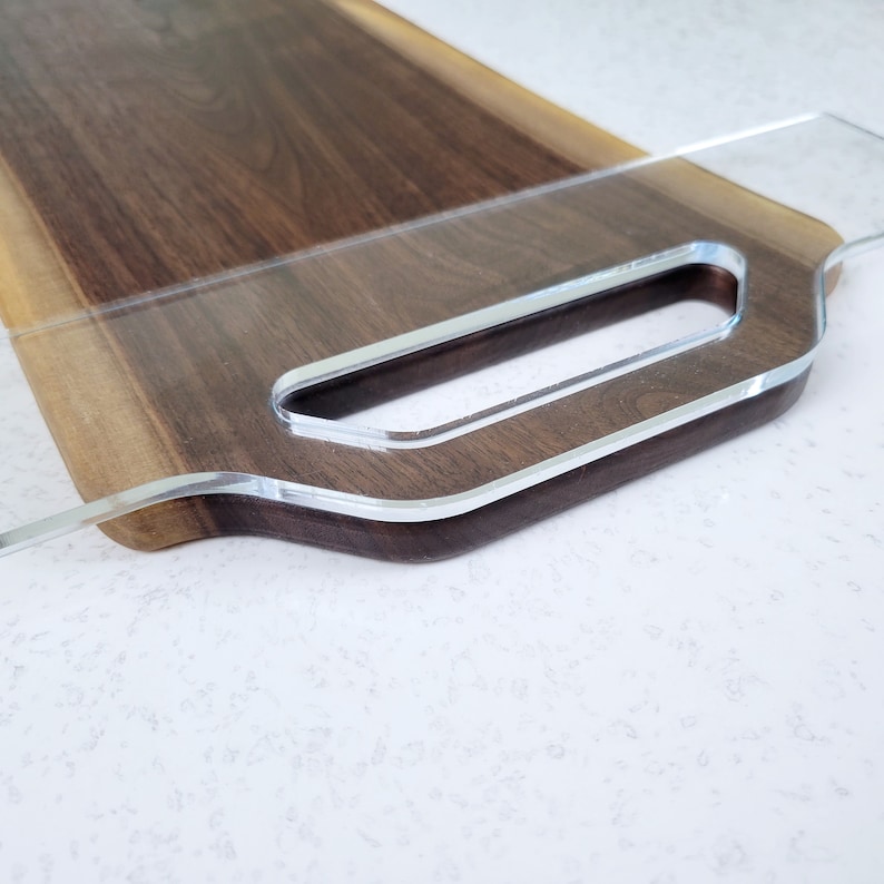 May include: A wooden serving tray with a clear acrylic handle. The tray is made of dark wood with a natural edge.