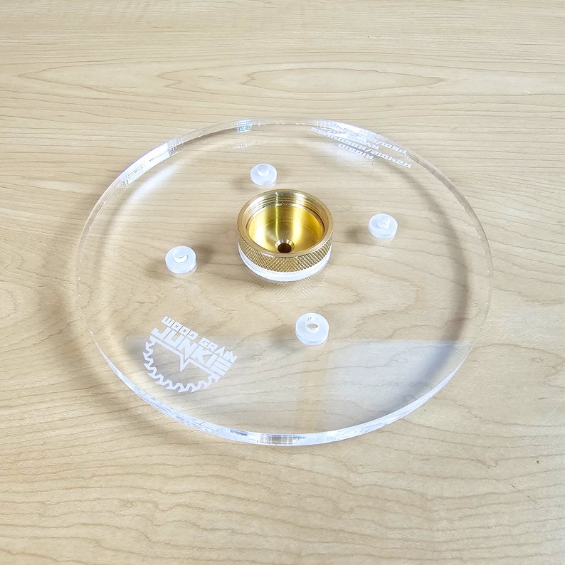Puede incluir: Una base de router de acr&iacute;lico transparente con un inserto central de lat&oacute;n y cinco insertos de pl&aacute;stico blanco. La base est&aacute; etiquetada como "Wood Grain Junkie".