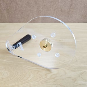Puede incluir: Una plantilla de router de pl&aacute;stico transparente con un inserto de lat&oacute;n y un mango negro. La plantilla tiene varios agujeros para diferentes tama&ntilde;os de fresas de router.
