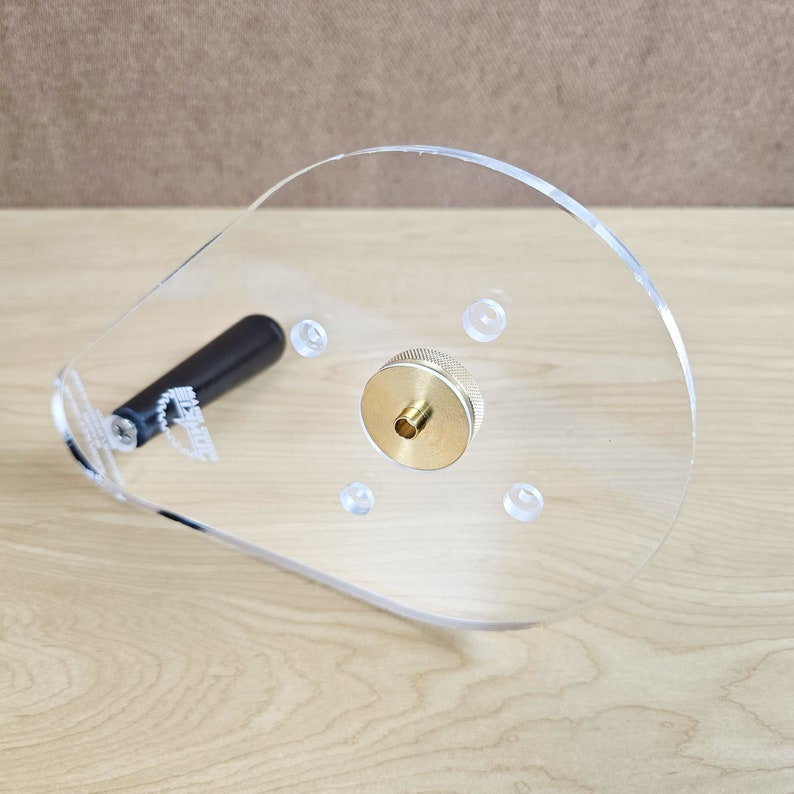 Puede incluir: Una plantilla de router de pl&aacute;stico transparente con un inserto de lat&oacute;n y un mango negro. La plantilla tiene varios agujeros para diferentes tama&ntilde;os de fresas de router.