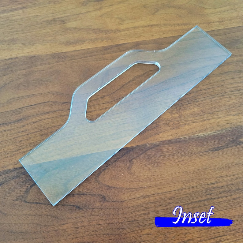 May include: A clear plastic template with a handle cutout. The template is designed for creating an inset, as indicated by the word "Inset" printed in blue on the wooden surface.