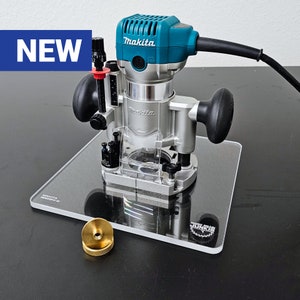 May include: A blue and silver Makita router with a clear plastic base, sitting on a clear acrylic base with the text "GOOD GEAR JUNKIE" printed on it. The router is new and has a black cord.