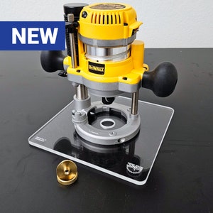 May include: A yellow and black DeWalt router is mounted on a clear acrylic base with a black circle in the center. The router has a black handle and a black switch. The base has the text "JONZEE" printed on it. A small gold metal piece is in the foreground.