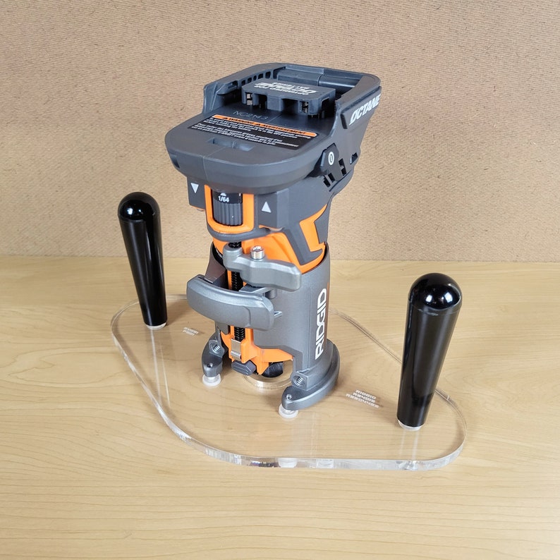 Pu&ograve; includere: Una fresatrice cordless nera e arancione con una base in acrilico trasparente e due manici neri. La fresatrice &egrave; etichettata "RIDGID OCTANE".