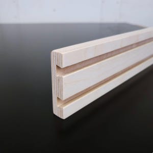 May include: Close-up of a light wood shelf with two grooves running along the length. The shelf is made of plywood and has a natural wood finish.