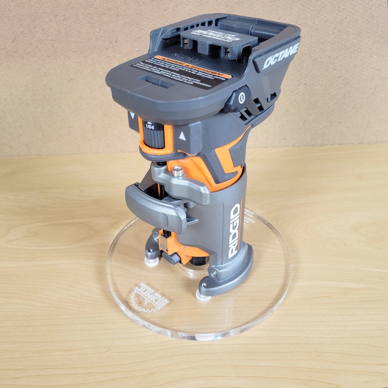 Puede incluir: Una fresadora inal&aacute;mbrica negra y naranja con una base de pl&aacute;stico transparente. La fresadora tiene una bater&iacute;a en la parte superior y el texto "OCTANE" y "RIDGID" en el lateral.
