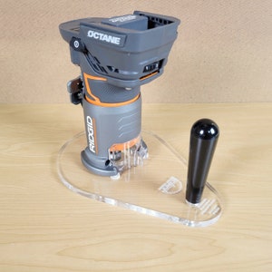 Puede incluir: Una fresadora inal&aacute;mbrica gris y naranja con una base de pl&aacute;stico transparente y un mango negro. La fresadora est&aacute; sentada sobre una base de pl&aacute;stico transparente con el texto "RIDGID" impreso en ella. La fresadora est&aacute; etiquetada como "OCTANE".