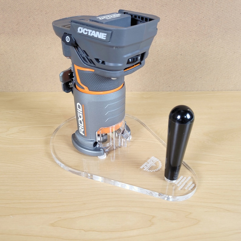 Puede incluir: Una fresadora inal&aacute;mbrica gris y naranja con una base de pl&aacute;stico transparente y un mango negro. La fresadora est&aacute; sentada sobre una base de pl&aacute;stico transparente con el texto "RIDGID" impreso en ella. La fresadora est&aacute; etiquetada como "OCTANE".