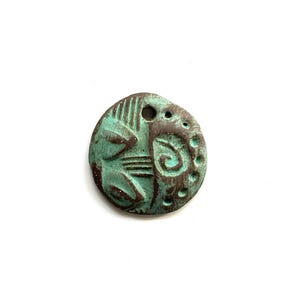 May include: A round, weathered pendant with a turquoise and brown patina. The pendant features etched patterns, including lines, dots, and a spiral design. It has a hole at the top for stringing.