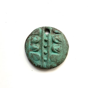 May include: A round, turquoise-colored pendant with a hole at the top for hanging. The pendant has a textured surface with a central vertical line of small circles and three sets of curved shapes on each side.