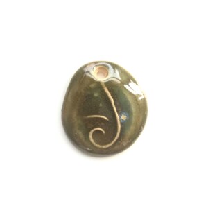 May include: A green ceramic pendant with a white swirl design. The pendant has a hole at the top for hanging.