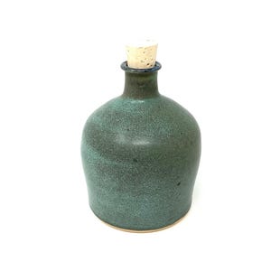Könnte beinhalten: Eine handgefertigte, teal-farbene Keramikflasche mit einem Korken. Die Flasche hat einen abgerundeten Körper und einen schmalen Hals. Der Korken hat eine hellbraune Farbe. Die Flasche wird wahrscheinlich zur Aufbewahrung von Flüssigkeiten verwendet.