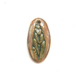 May include: An oval ceramic pendant featuring a glossy finish with a central sage green embossed leaf pattern. The outer border is a mottled blend of warm brown and cream tones. A small circular hole is positioned at the top for suspension.