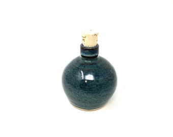 Peut inclure: Une bouteille ronde en céramique artisanale avec un glaçage bleu sarcelle moucheté. Elle est dotée d'un bouchon en liège et d'un bord bleu foncé. La bouteille mesure environ 10 cm de haut, idéale pour stocker des liquides ou comme pièce décorative.