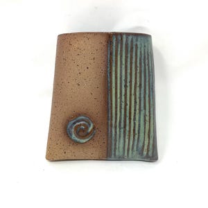 May include: A handcrafted ceramic vase with a unique design. The vase features a two-tone color scheme, with a speckled brown on one side and vertical teal stripes on the other. A blue swirl accentuates the brown side.