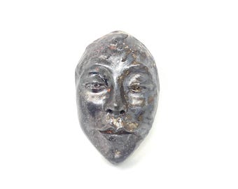 Könnte beinhalten: Keramik-Gesichtsskulptur mit metallisch silbernem und schwarzem Finish. Die Skulptur weist detaillierte Gesichtszüge auf, darunter Augen, Nase und Mund. Das Kunstwerk ist vor einem weißen Hintergrund platziert.