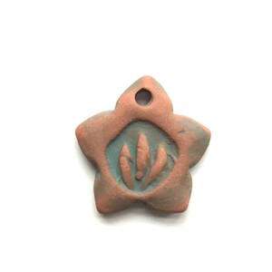 May include: A terracotta-colored ceramic star-shaped pendant with a blue-green glaze and a carved design of three leaves inside a circle.