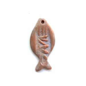 May include: A terracotta fish pendant with a detailed design of leaves or branches. The pendant is a light brown color and has a hole at the top for hanging.
