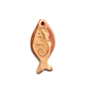 May include: A terracotta fish pendant with a white glaze and a brown swirl design. The pendant has a hole at the top for hanging.