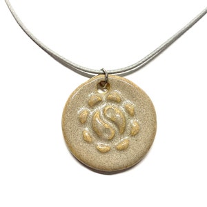 May include: A beige ceramic pendant necklace with a beige and white swirl design. The necklace is on a light gray cord.