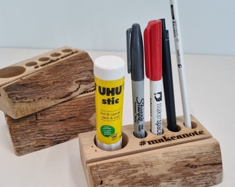 May include: Wooden desk organizer with five slots for pens and pencils. The organizer has the text "#makeanote" engraved on the front. There are four pens and a glue stick in the organizer.