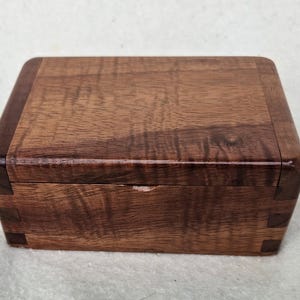 May include: A wooden box with a dark brown finish. The box has a hinged lid and is made of wood with a natural grain pattern.
