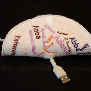 May include: A light gray, semi-circular felt pouch with a white snap closure and a USB cable. The pouch is embroidered with various names in different colors, including "Abba" and "Yahweh".