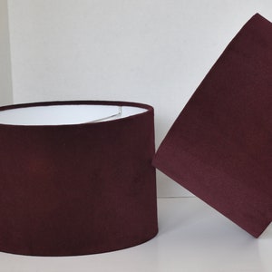 May include: Two burgundy lampshades made of fabric. The lampshades are cylindrical in shape and have a smooth, even texture.