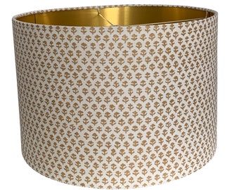 May include: A white drum lampshade with a gold floral pattern and a gold interior.