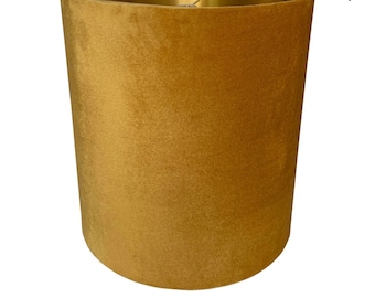 May include: A gold velvet lampshade with a gold metal top and bottom trim. The lampshade is cylindrical in shape and has a smooth, soft texture.